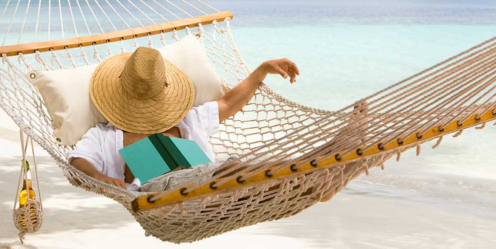 Man falling asleep while reading in a hammock on the beach